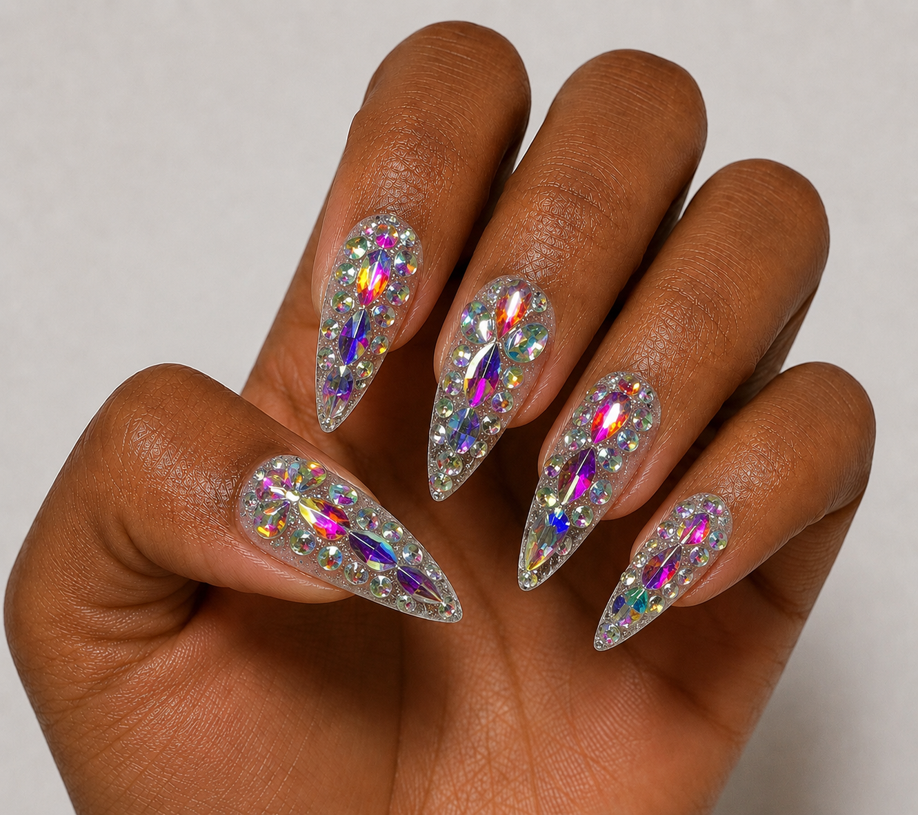 Hand with stiletto nails featuring rhinestone embellishments on a neutral background