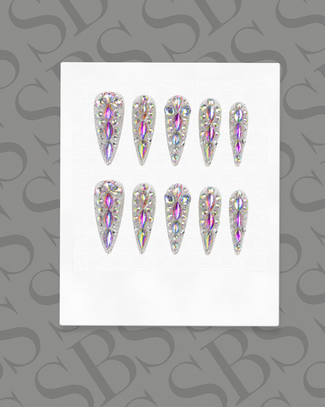 Set of rhinestone press-on nails on a white card with a gray background featuring a pattern.