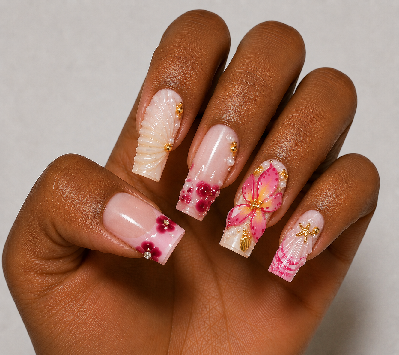 Hand with intricately designed nails featuring flowers, seashell and gold accents on a neutral background