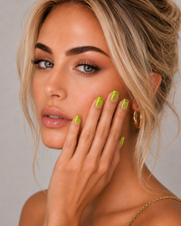 Woman with lime green ShadedbyShanell jelly press-on nails and gold hoop earrings against a neutral background