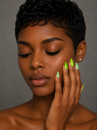 Black woman with short black hair and green ShadedbyShanell press-on nails touching her face against a gray background